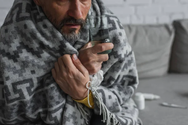 Partial view of man wrapped in warm blanket holding glass of water — Stock Photo