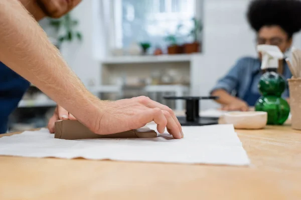 Cropped view of man pressing clay piece with hand near african american woman — Stock Photo