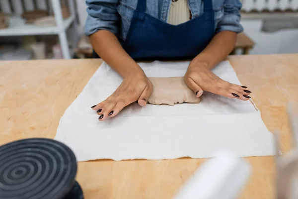Vista ritagliata di donna afro-americana in grembiule premendo pezzo di argilla con le mani in laboratorio di ceramica — Foto stock