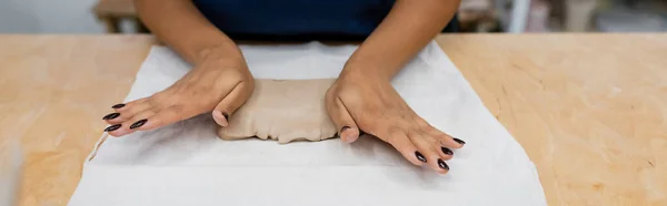 Cropped view of african american woman in apron pressing clay piece with hands during pottery class, banner — Stock Photo