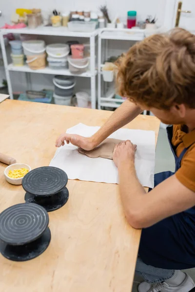 Высокий угол обзора рыжеволосый человек в фартуке нажатием кусок глины с рукой во время класса керамики — стоковое фото