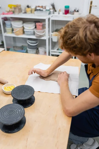 Vue grand angle de roux homme en tablier appuyant pièce d'argile avec la main pendant le cours de poterie — Photo de stock