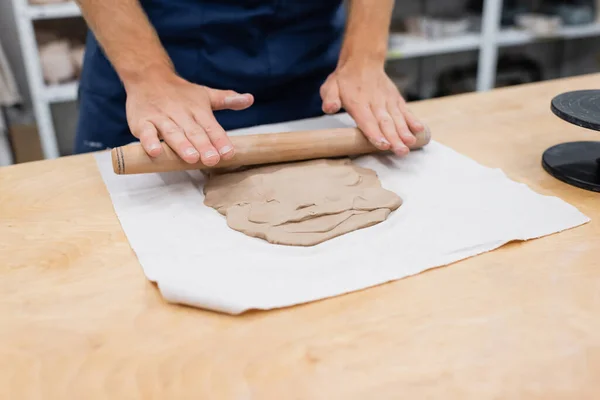 Vista cortada do homem no avental moldando peça de argila com rolo de pino durante a classe de cerâmica — Fotografia de Stock