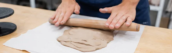 Vue recadrée de l'homme en tablier façonnant pièce d'argile avec rouleau à pâtisserie pendant la classe de poterie, bannière — Photo de stock