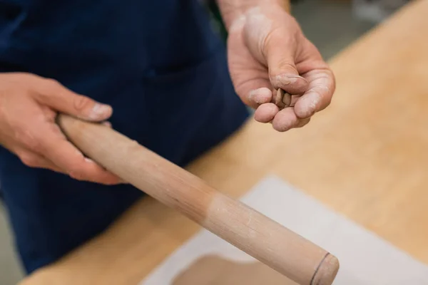 Cropped view of man holding wooden rolling pin and piece of clay in hands — Stock Photo