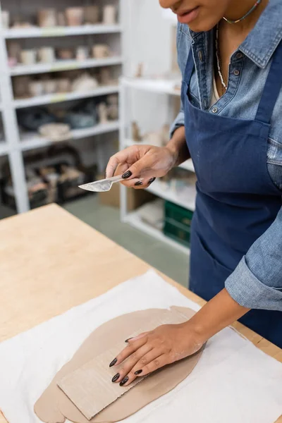 Vista recortada de mujer afroamericana sosteniendo cuchillo de arcilla cerca de cartón — Stock Photo