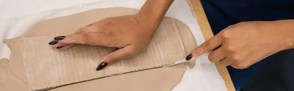 Vista superior de la mujer afroamericana que corta la arcilla con el cuchillo cerca del cartón, bandera — Stock Photo