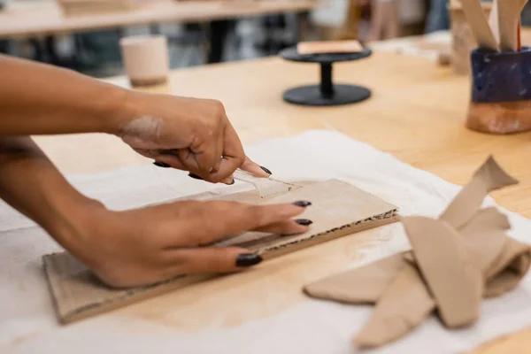 Partial view of african american woman cutting clay with knife while handcrafting in pottery workshop — Stock Photo