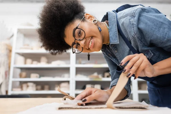 Felice donna africana americana in occhiali strappare cartone durante la classe di ceramica — Foto stock