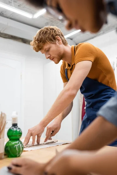 Man with red hair handcrafting near african american woman on blurred foreground — Stock Photo