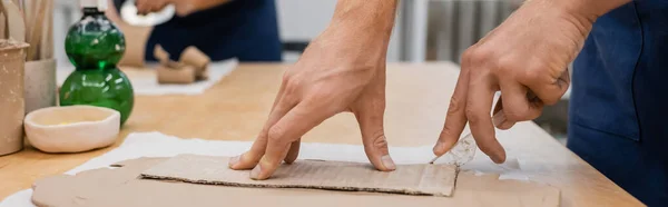 Abgeschnittene Ansicht eines Mannes, der in Töpferei Ton mit Messer um Karton schneidet, Banner — Stockfoto