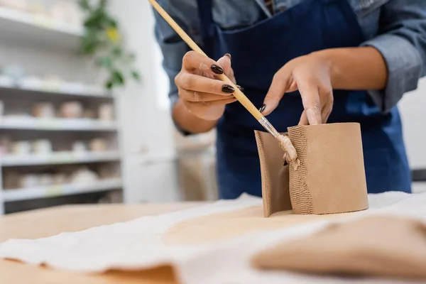 Cropped view of african american woman in apron holding shaper while modeling clay — Stock Photo