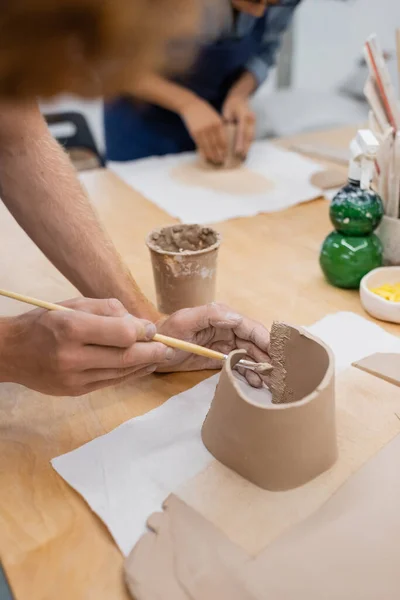 Vista ritagliata dell'uomo che tiene shaper mentre modella argilla durante la classe di ceramica — Foto stock