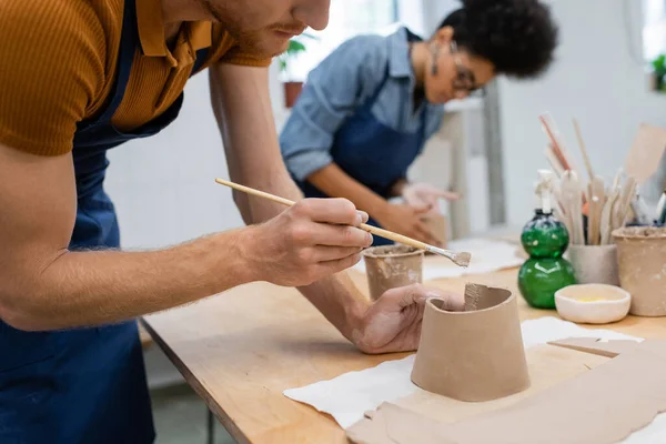 Vue recadrée de l'homme barbu tenant shaper tout en modélisant l'argile pendant la classe de poterie — Stock Photo