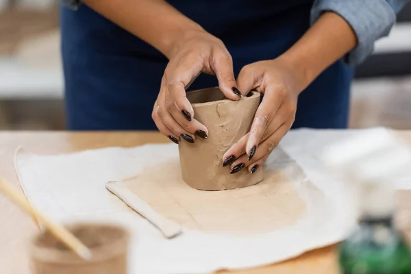 Vue partielle femme afro-américaine avec manucure façonnant l'argile pendant le cours de poterie — Photo de stock