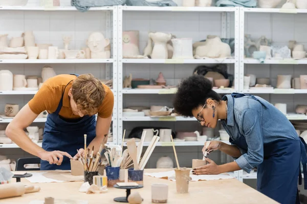 Femme multiethnique et homme façonnant des tasses d'argile pendant le cours de poterie — Photo de stock