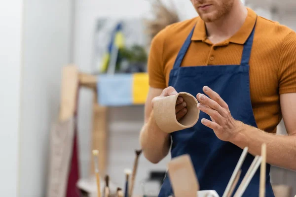 Vista ritagliata dell'uomo con barba modellare pezzo di argilla in tazza durante la classe di ceramica — Foto stock