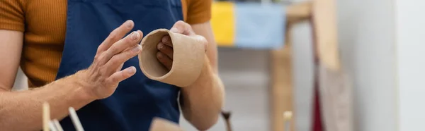 Vista recortada del hombre en delantal que forma la pieza de arcilla en taza durante la clase de cerámica, bandera — Stock Photo