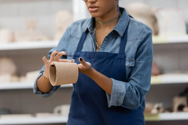 Vista parziale di donna afro-americana con tazza di argilla modellante manicure in laboratorio di ceramica — Foto stock