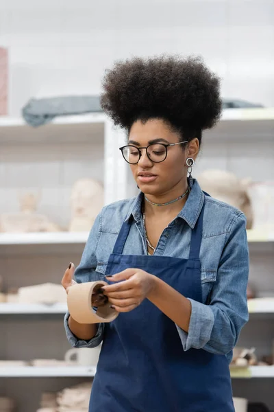 Femme afro-américaine bouclée avec manucure et cheveux bouclés modèle tasse d'argile dans l'atelier de poterie — Photo de stock