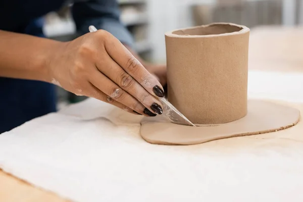 Vista cortada de mulher afro-americana cortando argila em torno de copo em forma com faca durante a classe cerâmica — Stock Photo
