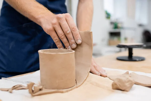 Vue recadrée de l'homme tenant un morceau d'argile tranché près d'une tasse en forme — Photo de stock