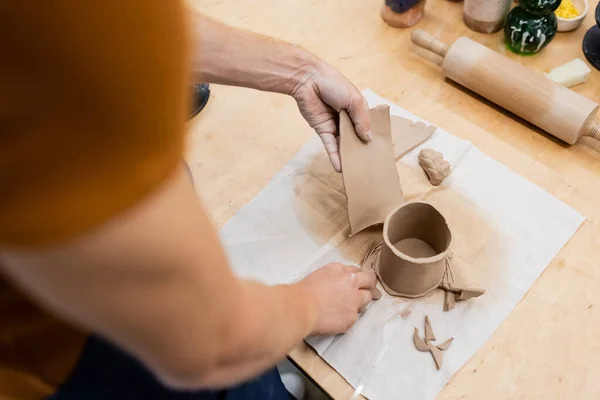 Vue de dessus de l'homme tenant un morceau tranché d'argile près de la tasse en forme et du rouleau à pâtisserie — Photo de stock