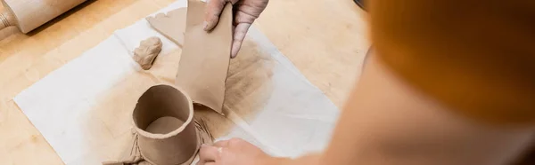 Top view of man holding sliced piece of clay near shaped cup and rolling pin, banner — Stock Photo