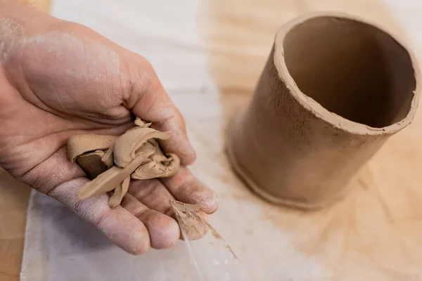 Vue recadrée de l'homme tenant des morceaux tranchés d'argile près d'une tasse en forme — Photo de stock