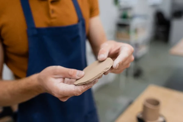 Cropped view of man in apron holding sliced piece of clay in hands — Stock Photo