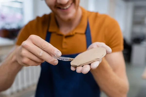 Cropped view of cheerful man in apron holding sliced piece of clay and shaper — Stock Photo