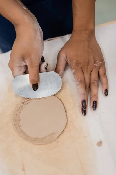 Top view of african american woman with manicure holding steel scraper while shaping clay piece — Stock Photo