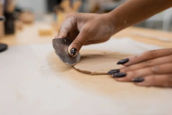 Abgeschnittene Ansicht einer afrikanisch-amerikanischen Frau mit Maniküre, die einen Edelstahlschaber hält, während sie Ton formt — Stockfoto