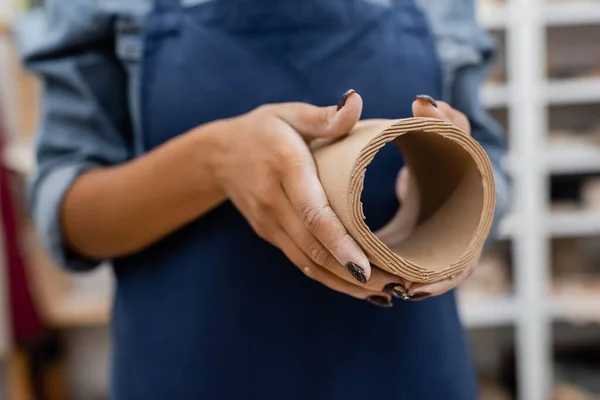 Partial view of african american woman in apron holding circle shape clay piece in hands — Stock Photo