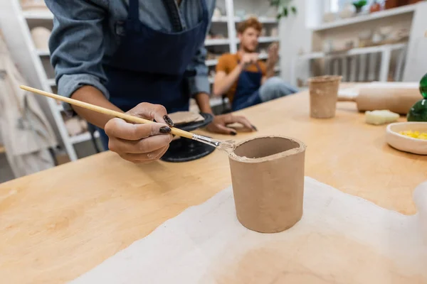 Abgeschnittene Ansicht einer afrikanisch-amerikanischen Frau, die Shaper hält, während sie Tonbecher in der Nähe eines verschwommenen Mannes modelliert — Stockfoto