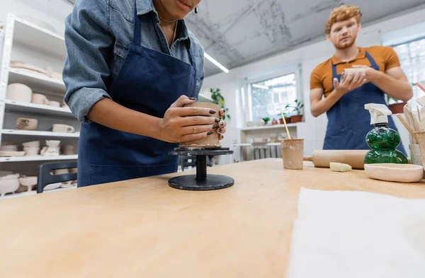 Afroamerikanerin formt Tonbecher in der Nähe von verschwommenem und rothaarigem Mann — Stockfoto