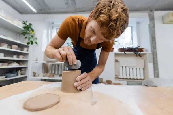 Young and redhead man holding stainless steel scraper while shaping clay cup — Stock Photo