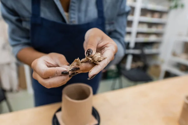 Vue recadrée d'une femme afro-américaine tenant des morceaux d'argile tranchés près d'une tasse en forme — Photo de stock