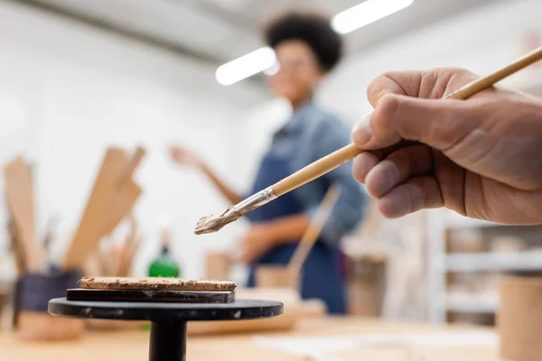 Cropped view of man holding shaper in hand near flat clay piece and blurred african american woman — Stock Photo