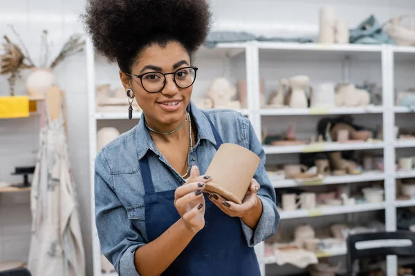 Positive und lockige afrikanisch-amerikanische Frau im Schürzenschürzen-Ton-Becher in den Händen — Stockfoto