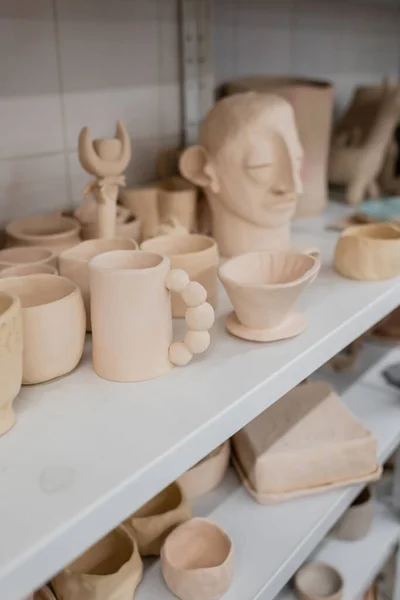 Different clay sculptures near cups on shelves of pottery shop — Stock Photo