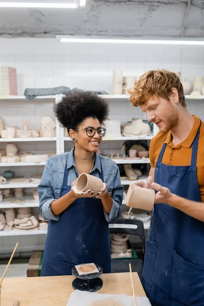 Fröhliches gemischtrassiges Paar gießt Tonbecher bei Date im Töpferatelier — Stockfoto