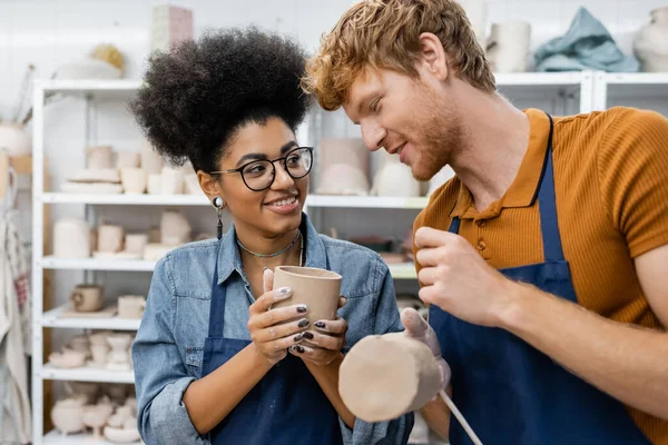 Feliz casal interracial moldando copos de barro durante a data no estúdio de cerâmica — Fotografia de Stock