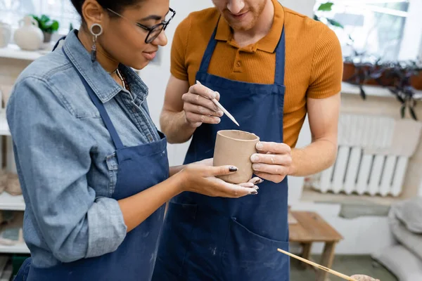 African american woman in eyeglasses looking at bearded redhead man modeling clay cup with shaper — Stock Photo