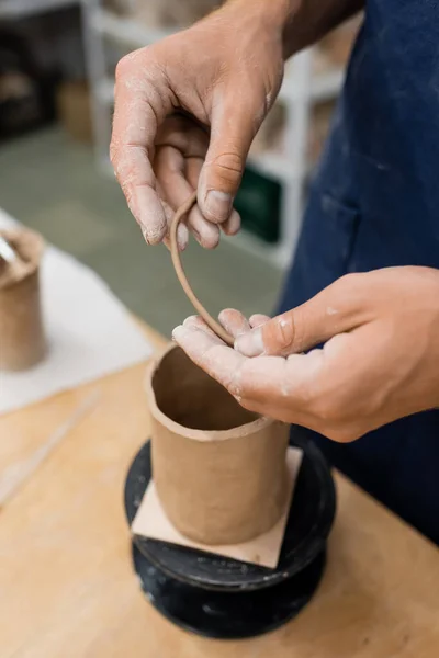 Ausgeschnittene Ansicht eines Mannes mit Ton in der Nähe einer verschwommenen Skulptur im Töpferatelier — Stockfoto