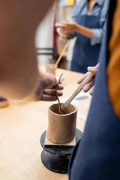 Vista ritagliata dell'uomo che tiene argilla e strumento in studio di ceramica — Foto stock