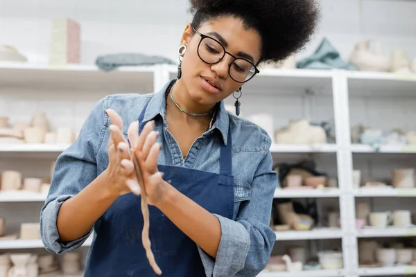 African american craftswoman in apron forming clay in blurred pottery workshop — Stock Photo