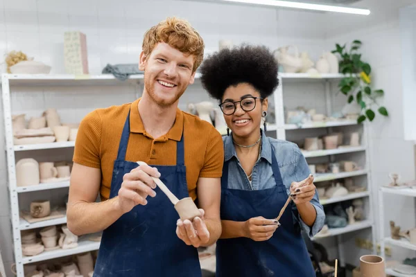 Smiling man and african american woman holding clay in pottery workshop — Stock Photo