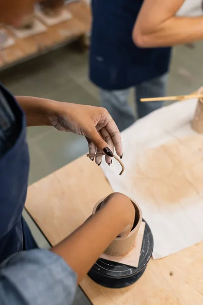 Vue recadrée d'une femme afro-américaine tenant de l'argile près d'une sculpture dans un atelier de poterie — Photo de stock