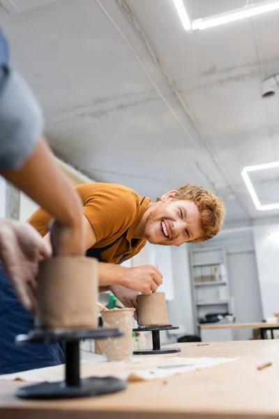 Cheerful man looking at blurred african american girlfriend in pottery studio — Stock Photo